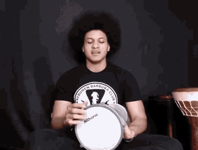 a man with an afro is playing a tambourine while sitting in a lotus position .