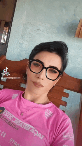 a woman wearing glasses and a pink shirt is sitting on a chair .