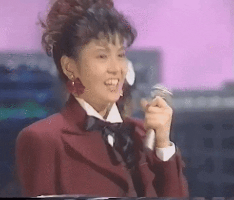 a woman is singing into a microphone while wearing a red suit and bow tie .