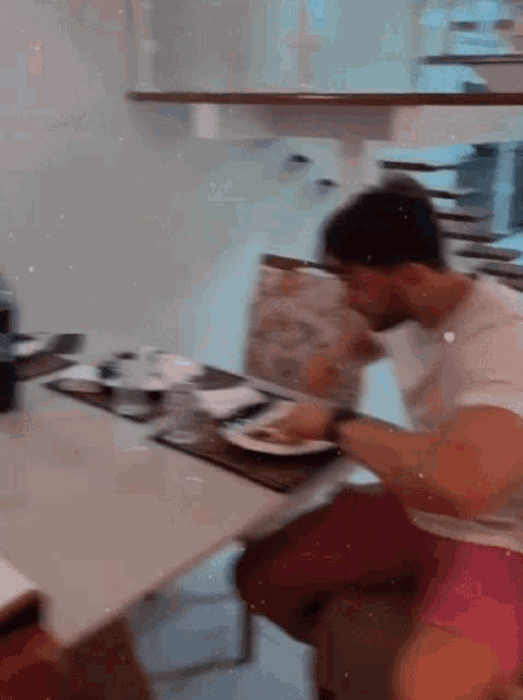 a man in a white shirt sits at a table with a plate of food on it