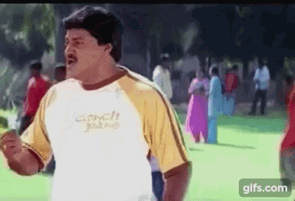 a man in a yellow and white t-shirt is standing in a park .
