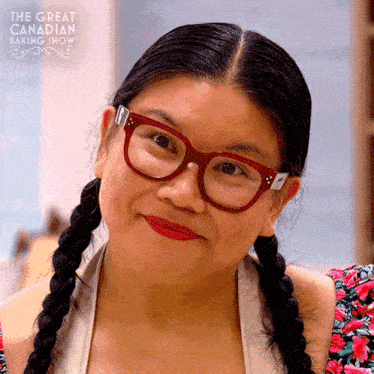 a woman wearing pigtails and glasses is smiling in front of a sign that says the great canadian baking show