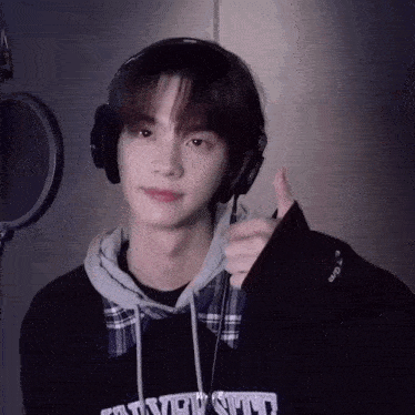 a young man wearing headphones and a sweatshirt that says university giving a thumbs up