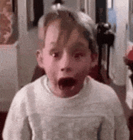 a young boy in a sweater is making a surprised face .