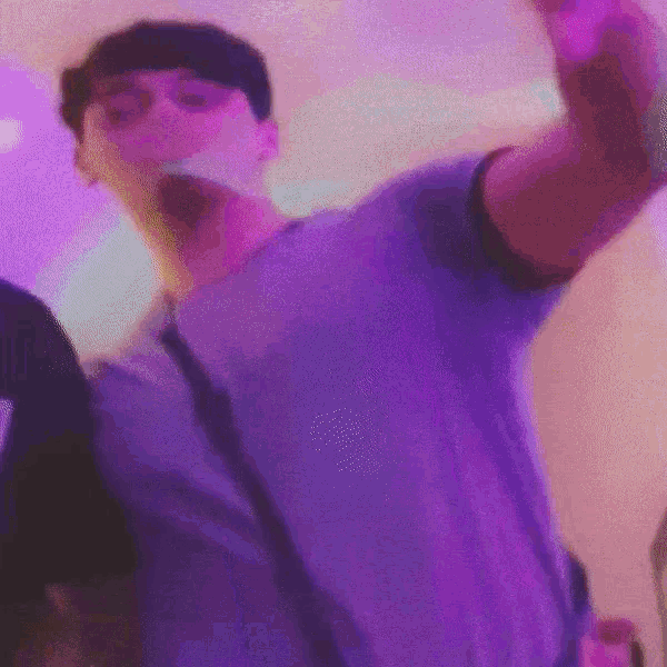 a man in a purple shirt is dancing in a room with purple lights