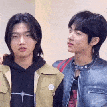 two young men are standing next to each other in a room and looking at each other .