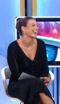 a woman in a black dress is sitting in a chair on a television show and laughing .