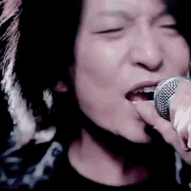 a close up of a man singing into a microphone with his eyes closed