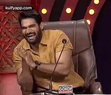 a man is sitting in a chair and laughing in front of a microphone .