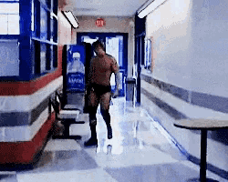 a man without a shirt is walking down a hallway with a pepsi machine in the background