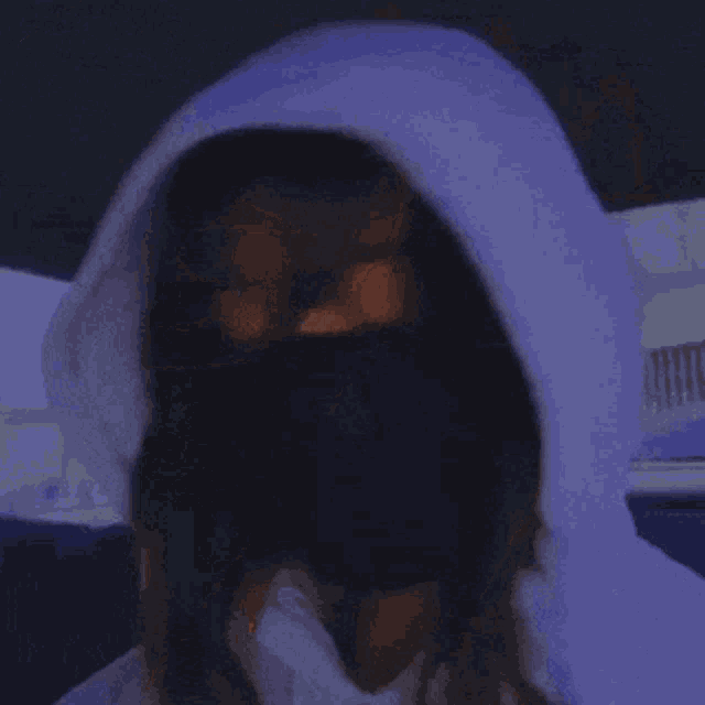 a woman wearing a black mask and a white hoodie is covering her face with her hands .