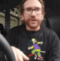 a man wearing glasses and a bart simpson shirt is driving a car .