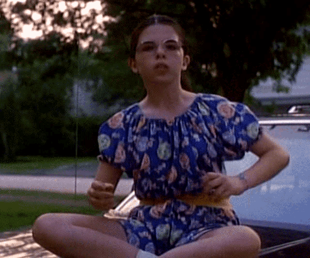 a woman in a blue dress is sitting on a car