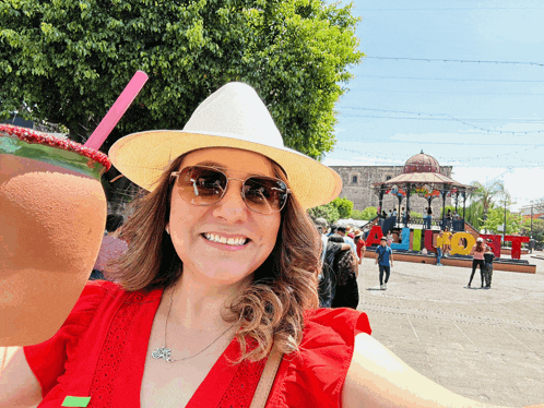a woman wearing a straw hat and sunglasses is holding a drink in front of a sign that says " mexico "
