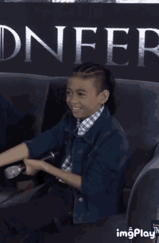 a young boy is sitting in front of a sign that says ' dnfer '