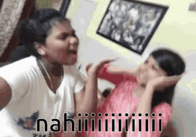 two girls are sitting next to each other in a room and one of them is covering her ears with her hands .