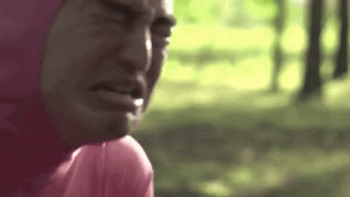 a man in a pink shirt is crying in a park .