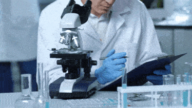 a scientist is looking through a microscope while writing on a clipboard