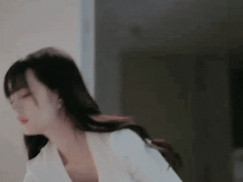 a woman in a white shirt is standing in a room with her eyes closed and her hair blowing in the wind .