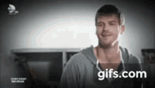 a man in a gray hoodie is smiling in a room .