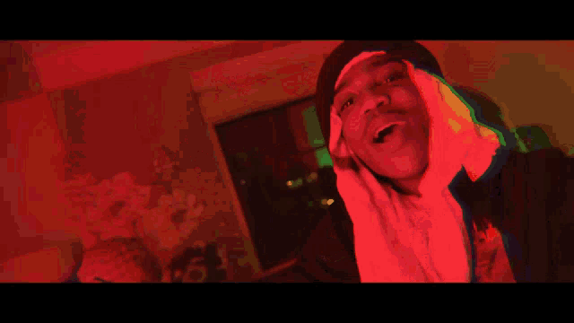 a man wearing a hooded sweatshirt and a beanie is standing in a room with red lights