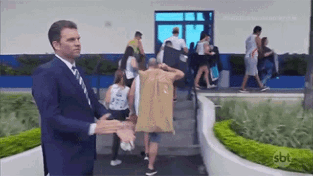 a man in a suit and tie is standing in front of a group of people walking down stairs .