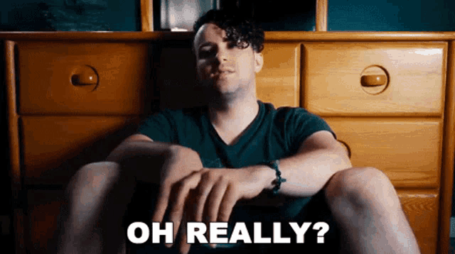 a man is sitting on a bed with his legs crossed and the words oh really written on the screen .