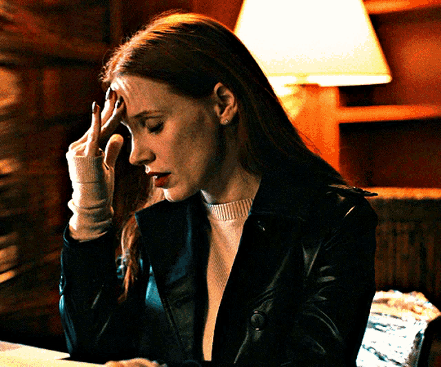 a woman holds her hand to her forehead while sitting at a table