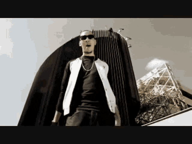 a man wearing sunglasses and a white vest is standing in front of a building .