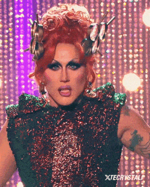 a drag queen is wearing a green and red sequined dress and has a tattoo on her arm ..