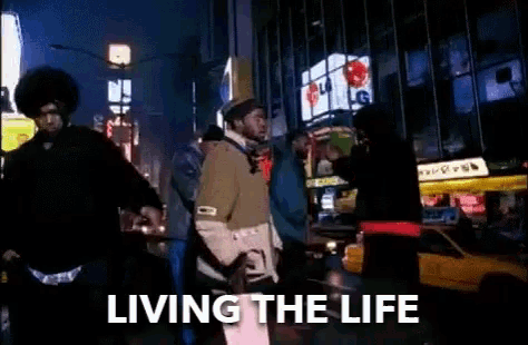 a group of people are walking down a city street at night with the words living the life written on the bottom .
