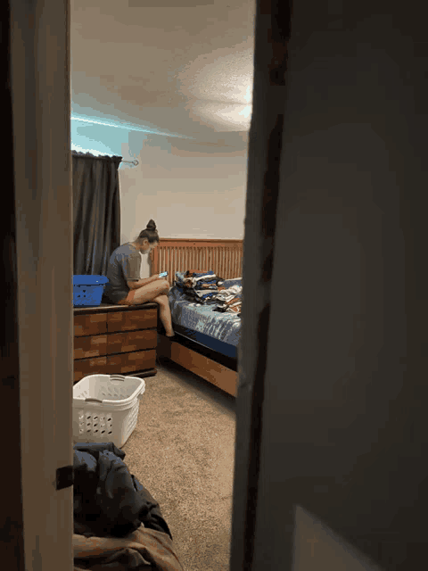 a woman sits on a dresser in a bedroom with a laundry basket on the floor