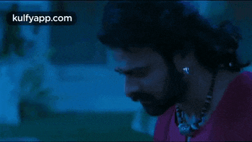 a man with a beard wearing a red shirt and a necklace is looking down .