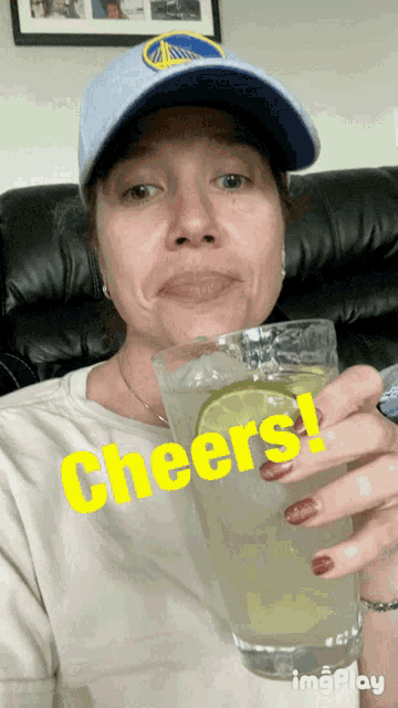 a woman wearing a golden state warriors hat is holding a glass of liquid with the words cheers written on it
