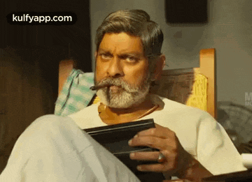 a man with a beard and mustache is smoking a cigar while sitting in a chair .