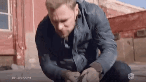 a man in a blue jacket is kneeling down on the ground in front of a building .