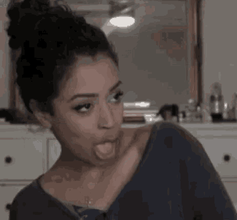 a woman is sticking her tongue out in front of a mirror while wearing a blue shirt .