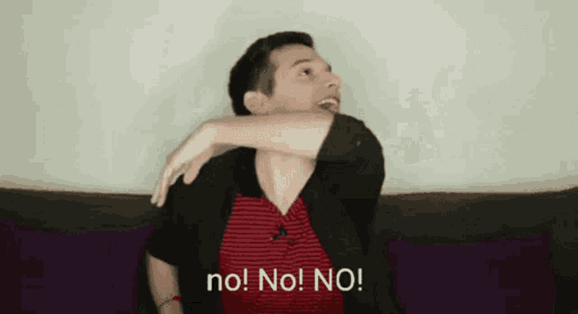 a man is sitting on a couch with his arm around his shoulder and says no ! no ! no !