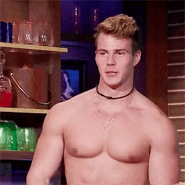 a shirtless man is standing in front of a shelf with wine glasses