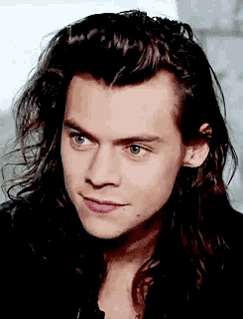 harry styles is wearing a black jacket and has long hair .