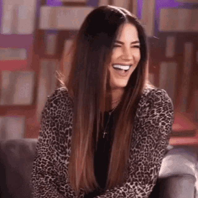 a woman is sitting on a couch wearing a leopard print jacket and smiling .