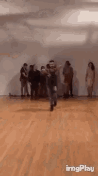 a group of people are standing in a room while a man is dancing on a wooden floor .