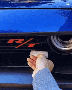a person is cleaning the front of a blue car with a red r on it