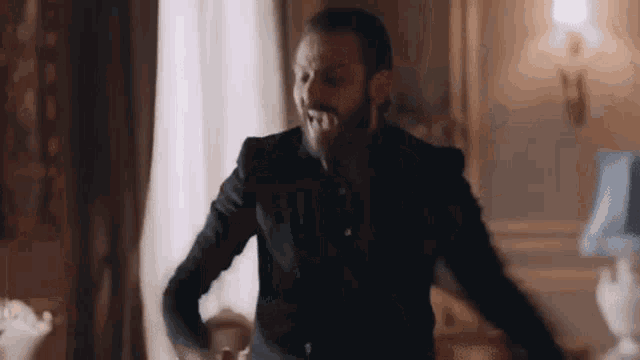 a man with a beard is wearing a suit and dancing in a living room .