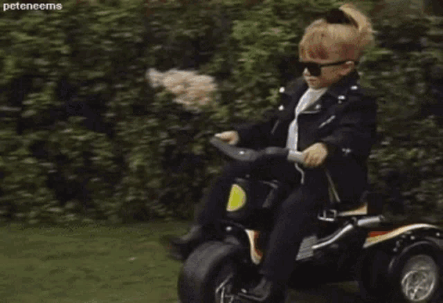 a young boy in a leather jacket and sunglasses is riding a toy motorcycle .