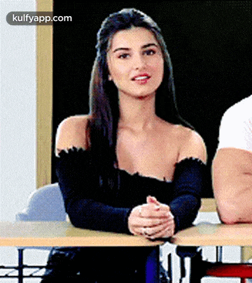 a woman in a black off the shoulder top is sitting at a desk .