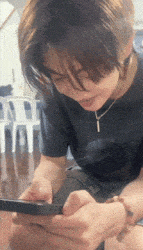 a young man wearing a black shirt and a necklace is playing a game on his phone