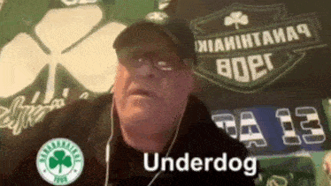 a man wearing headphones and a hat says underdog in front of a sign