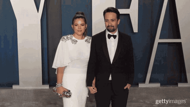 a man in a tuxedo and a woman in a white dress pose for a photo