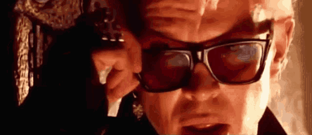 a man wearing sunglasses is holding a gun in his hand .
